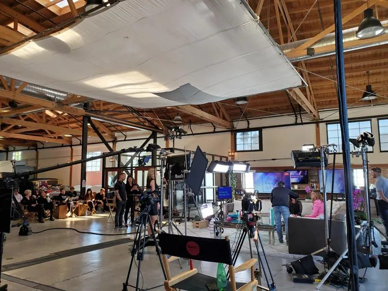 A timber-beam studio rigged with a large overhead silk and film lighting over a seated interview set.